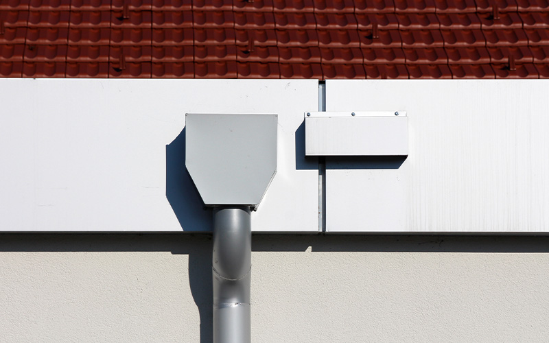 eaves of a modern building with a gray metal finish and white gutter piping under a cloudy sky showcasing three-dimensional architectural design